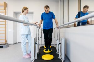 Physical therapist guiding a patient through balance training exercises using parallel bars and stability equipment during rehabilitation.