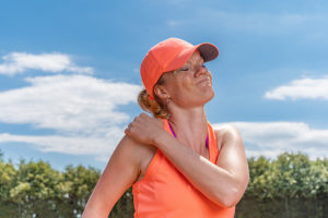 Woman on tennis court rubbing her painful shoulder