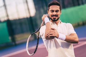 Man on tennis court holding his painful elbow