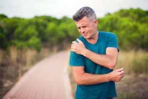 Athletic man on running trail holding his painful shoulder