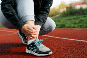 Female runner kneeling on the track and holding her painful sprained ankle