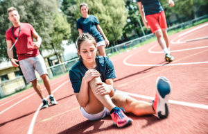 Young female runner sitting on track with a knee injury