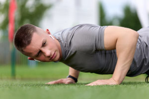 Young male athlete doing pushups on green playing field