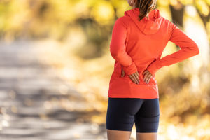 Female jogger paused on running path due to low back pain while thinking about seeking spine care