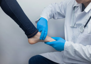Orthopedic surgeon wearing blue gloves examining a woman's foot for signs of plantar fasciitis