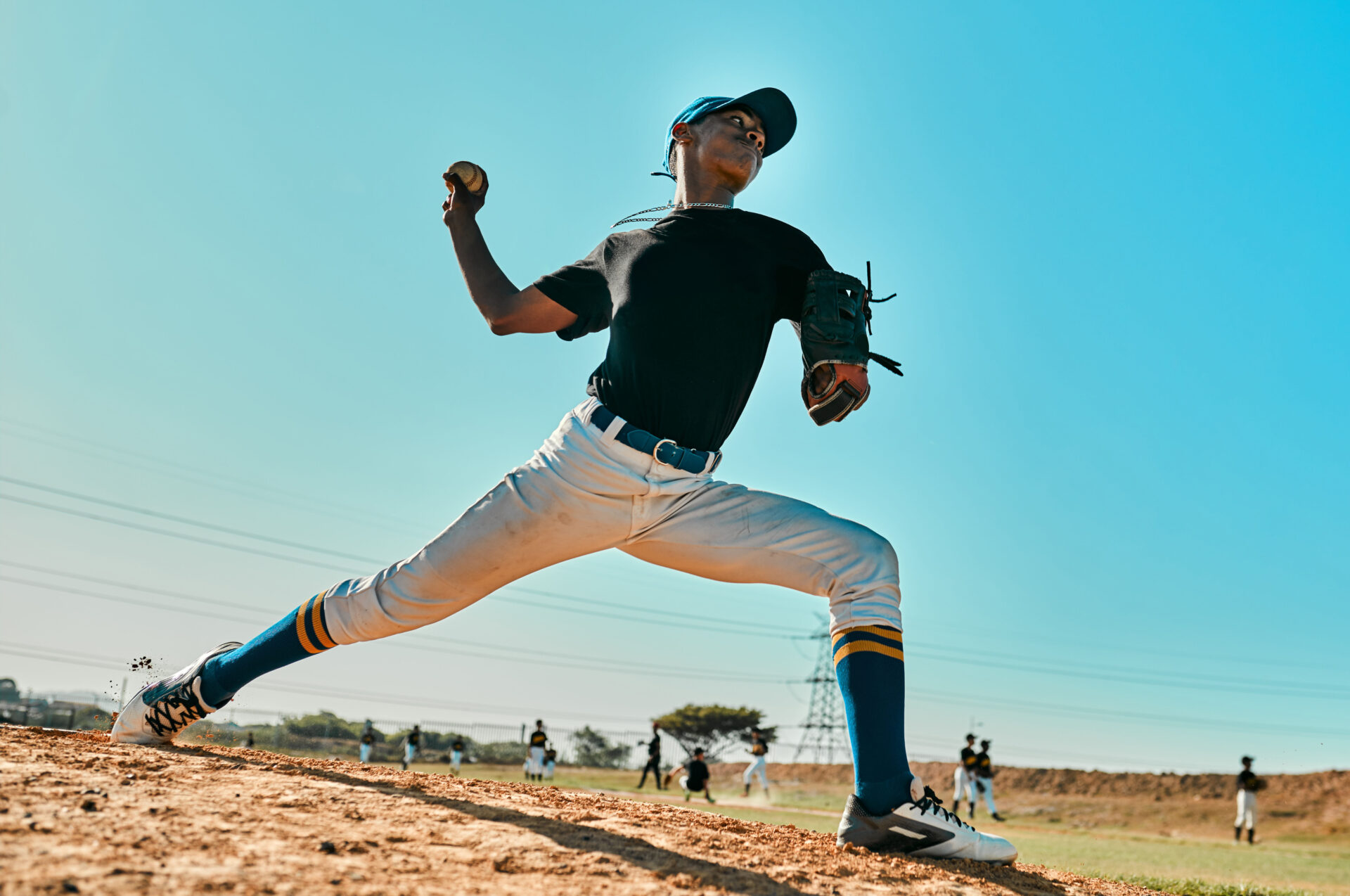 Shot of a young baseball player pitching the ball during a game outdoors. He is mid-throw.