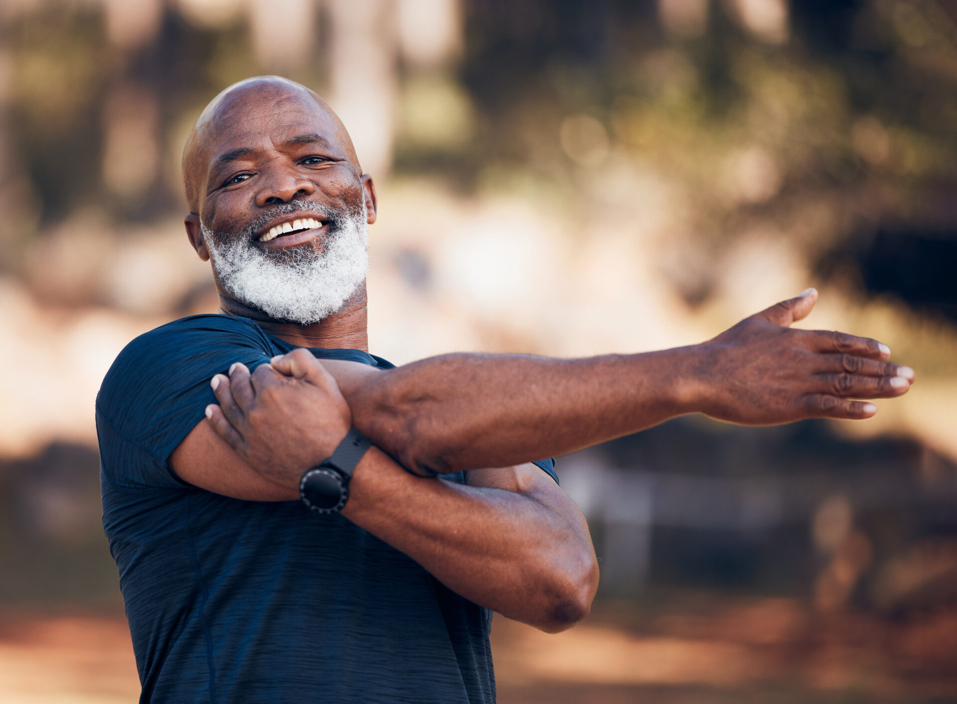 Elderly man is stretching his shoulder before exercising in the park outside. Man has recovered from a successful total shoulder replacement surgery. 