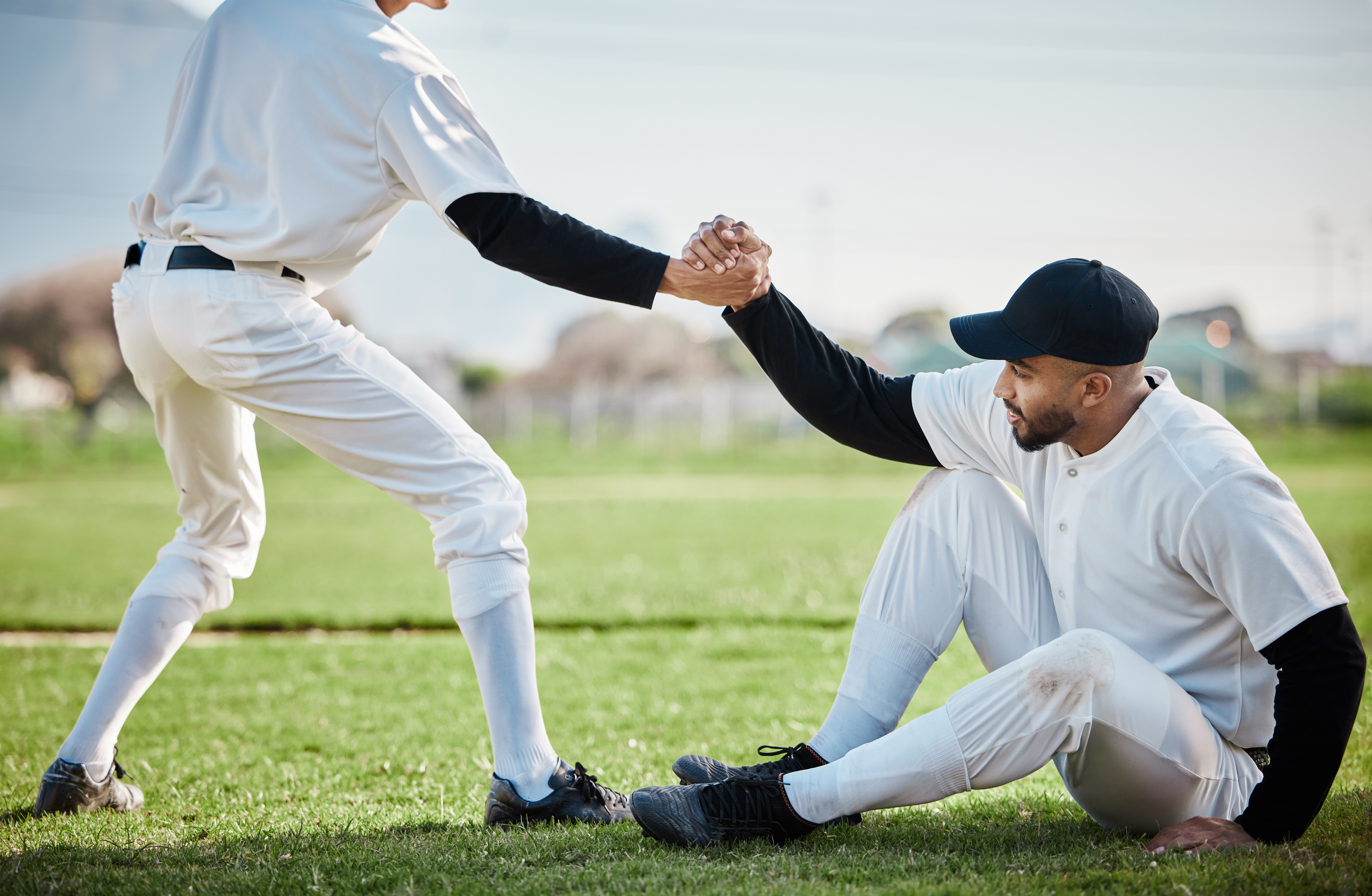 Baseball player extending hand out to help teammate off the ground. Baseball player has recovered from a total shoulder replacement surgery