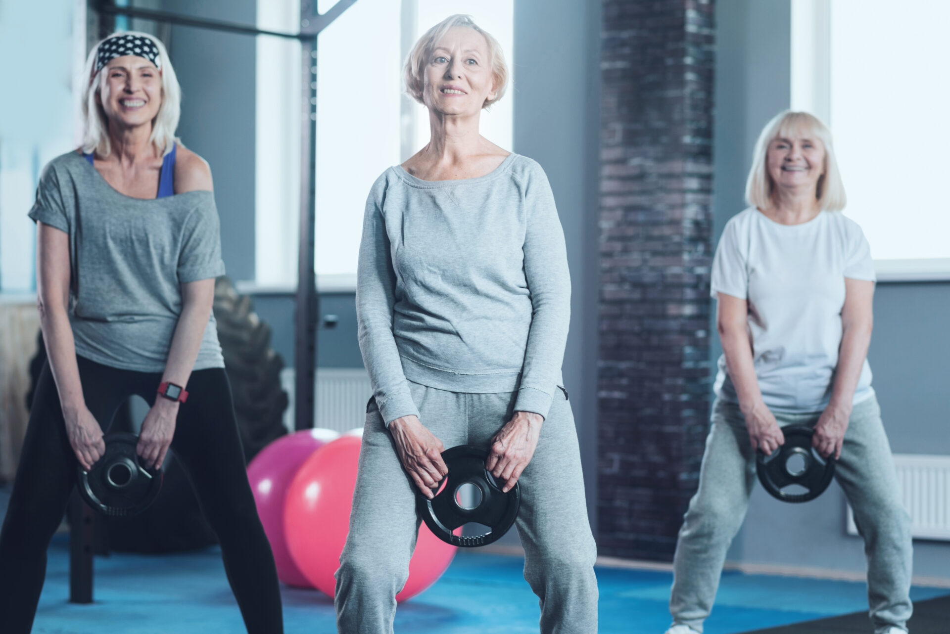 Motivated elderly ladies enjoying their training while lifting weight disks during a training class in a fitness club.