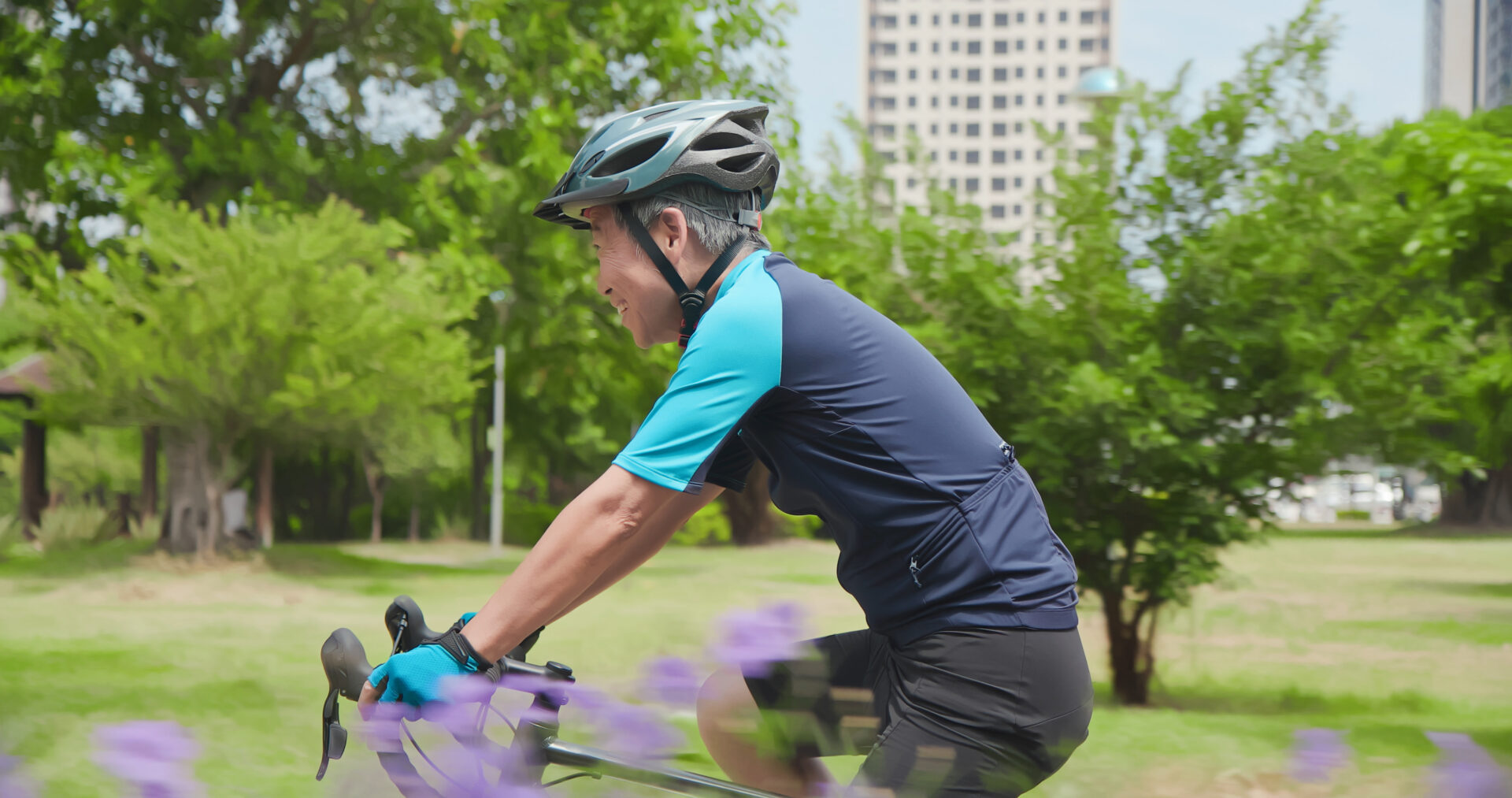 Sideview of Asian elderly man wearing helmet is cycling a bicycle in the park. He recently recovered from a successful total knee replacement surgery.