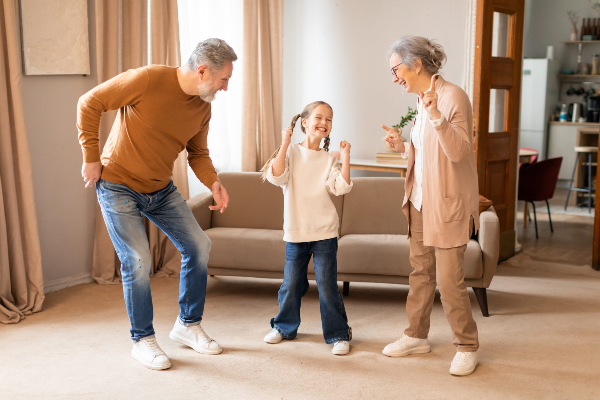 A young girl is gleefully dancing with her grandparents in the warmth of their living room, sharing a special moment of laughter and fun, all expressing happiness and the strong bond of family. Both grandparents have successfully recovered from total knee replacement surgeries.