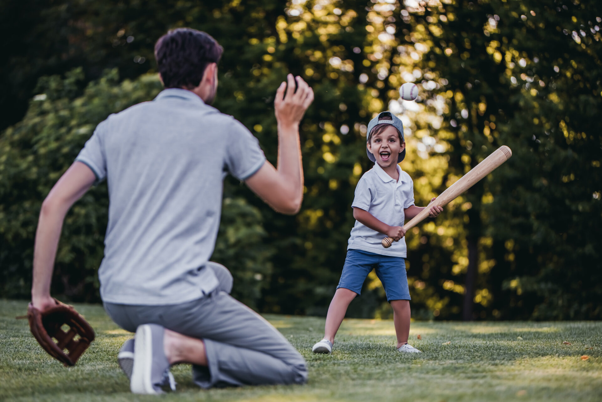 Father is throwing catch to his young son. Father is throwing baseball to son, who is holding a baseball bat, ready to swing. Father has recovered from successful shoulder instability and labral tear sugery