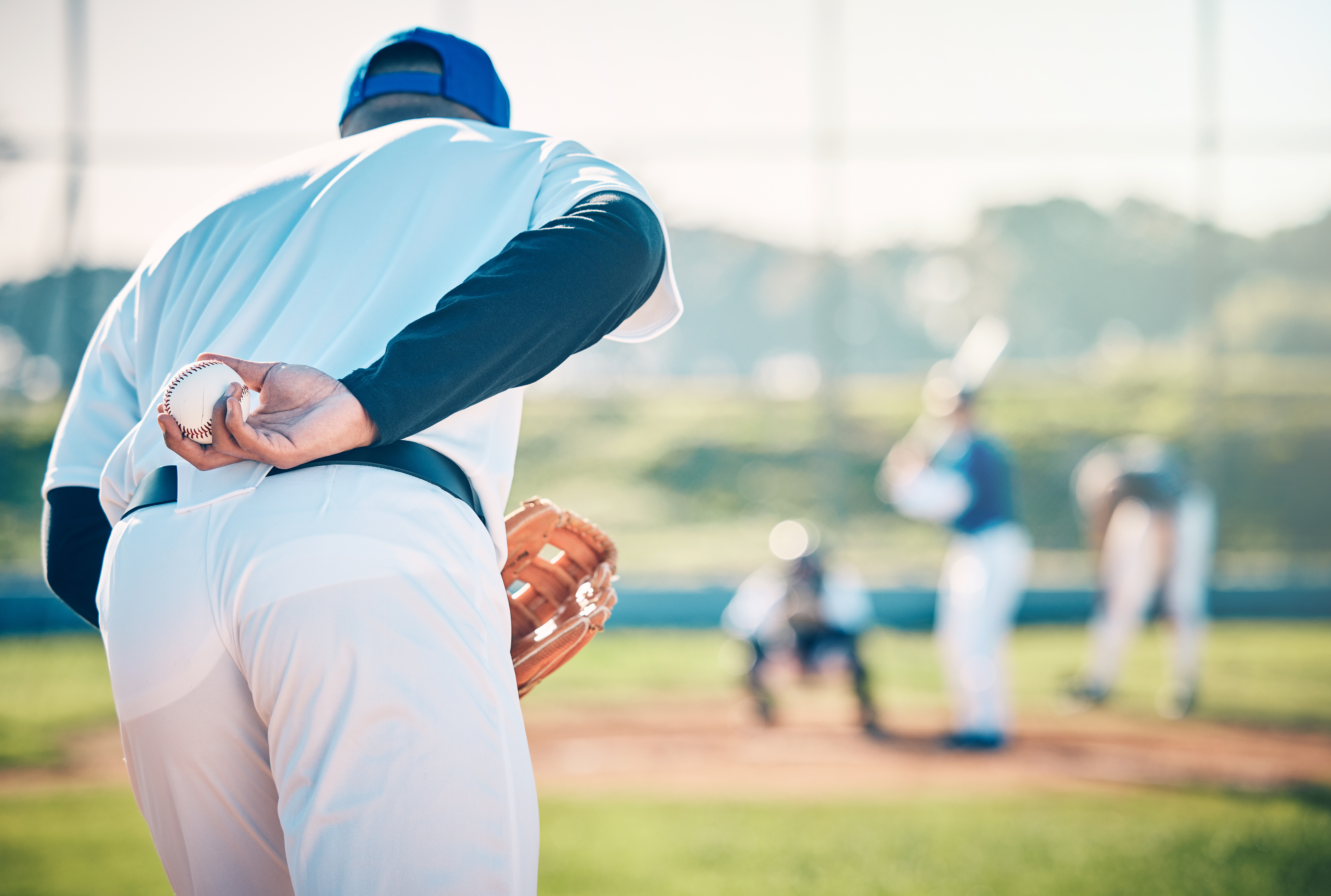 Male baseball pitcher with hand behind back with mitt in preparation for pitching baseball outdoors. Man has recovered from shoulder injury in baseball