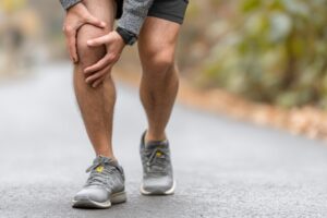 Man holding his knee while walking on pavement, illustrating knee cracking and possible knee pain during movement.