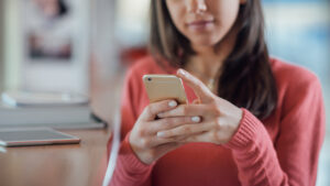 Young woman using smartphone while experiencing thumb and hand arthritis symptoms