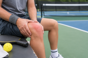 Adult seated with one hand near a swollen knee after recreational sports.
